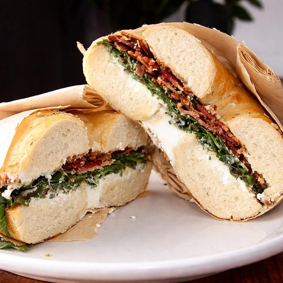 Two halves of a bagel sandwich filled with crispy bacon, green arugula, and cream cheese.